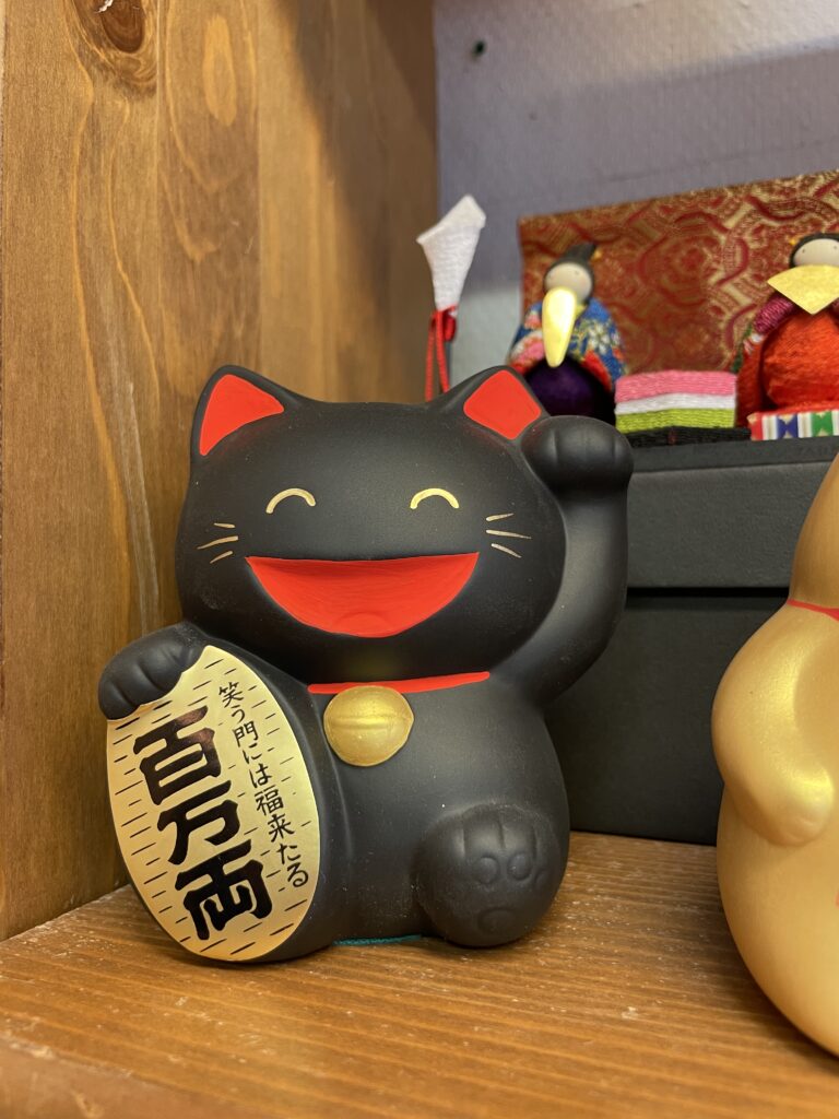 Maneki-neko noir avec sourire et patte levée, figurine japonaise porte-bonheur