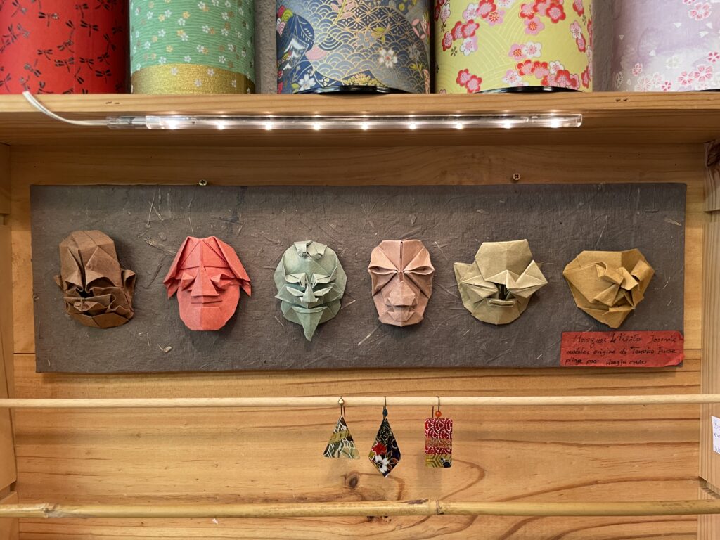 Origamis représentant des visages expressifs exposés avec des bijoux artisanaux