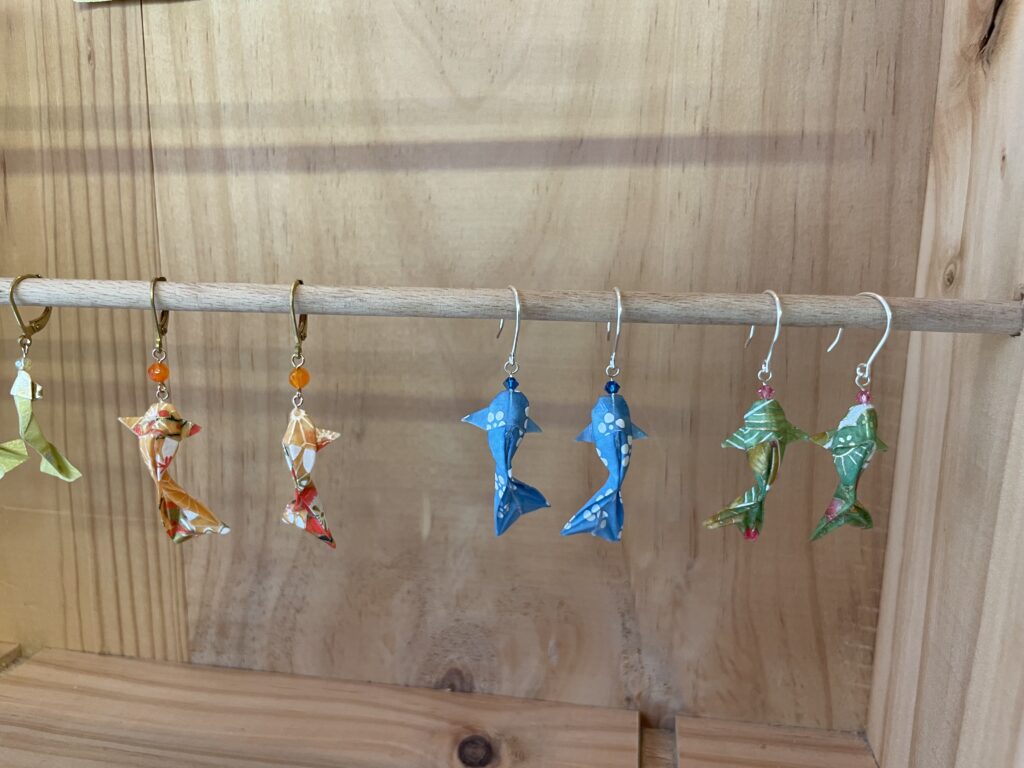 Boucles d’oreilles en forme de poissons réalisés en origami, suspendues sur une branche en bois